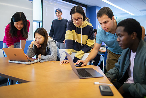 students in a classroom gathered around laptops